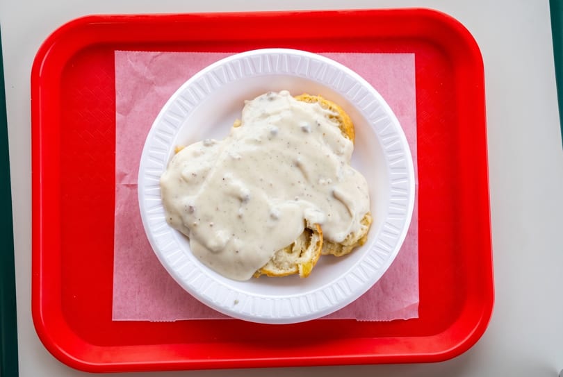 Biscuits and gravy on a white plate with a red tray and white paper liner.